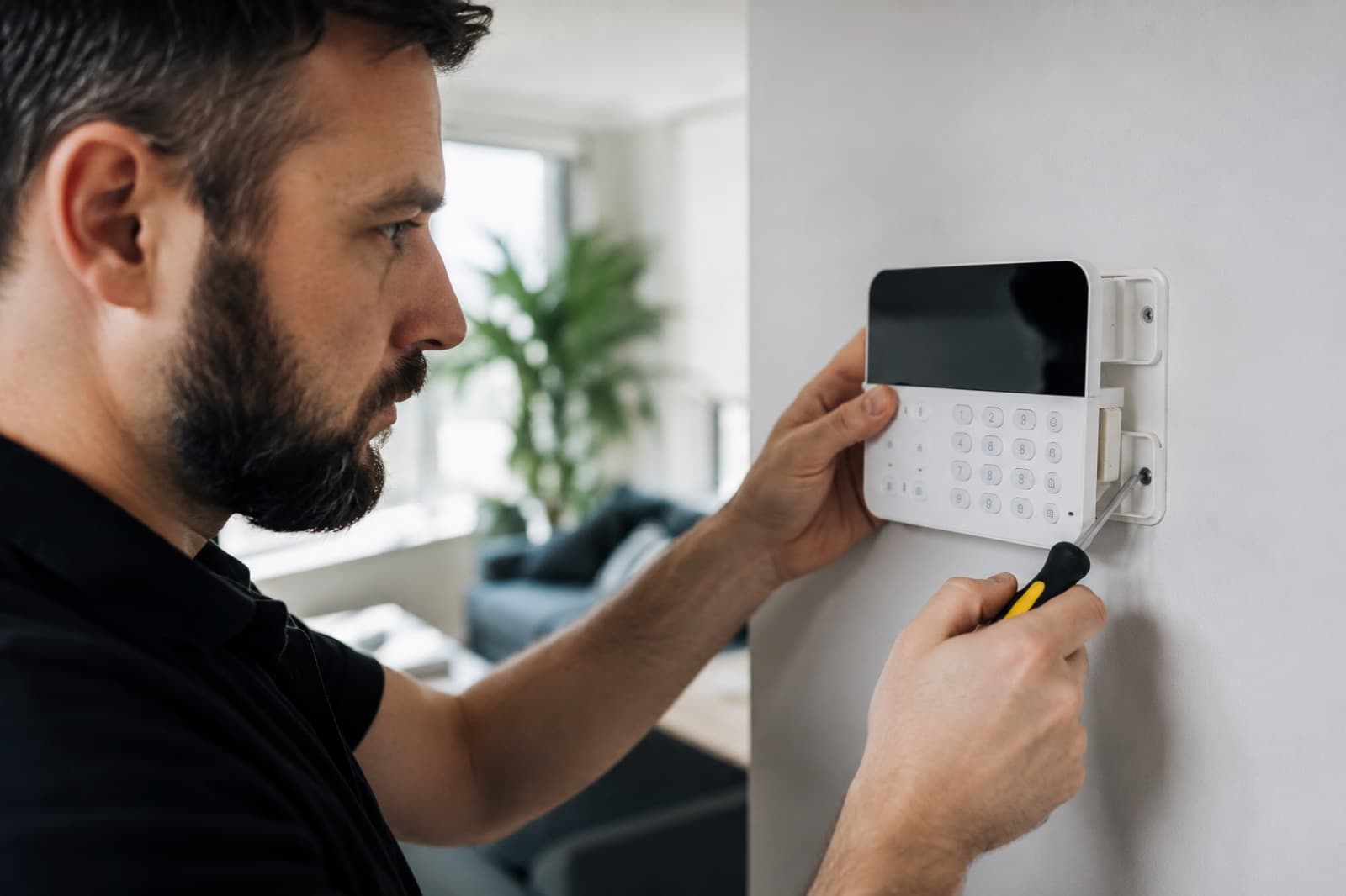 Techniker eines Fachbetriebs montiert ein Alarm-Bedienteil an der Wand